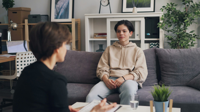 Eine Frau sitzt auf einer Couch und spricht mit einer anderen Frau, die ihr gegenüber sitzt