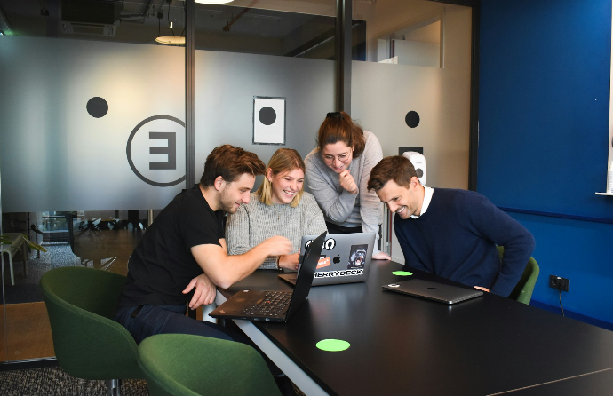 Vier Personen sitzen an einem Tisch um einen Laptop herum